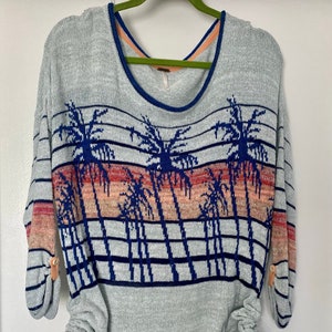 May include: A light blue sweater with a palm tree print and horizontal stripes. The sweater has a scoop neck and long sleeves with buttons on the cuffs. The bottom of the sweater has a drawstring with orange ties.