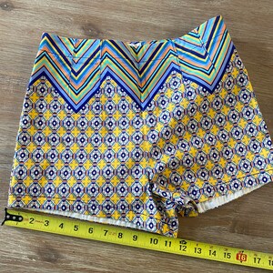 May include: Yellow and blue patterned shorts with a geometric design. The shorts have a zig-zag pattern at the top and a smaller geometric pattern on the rest of the shorts.