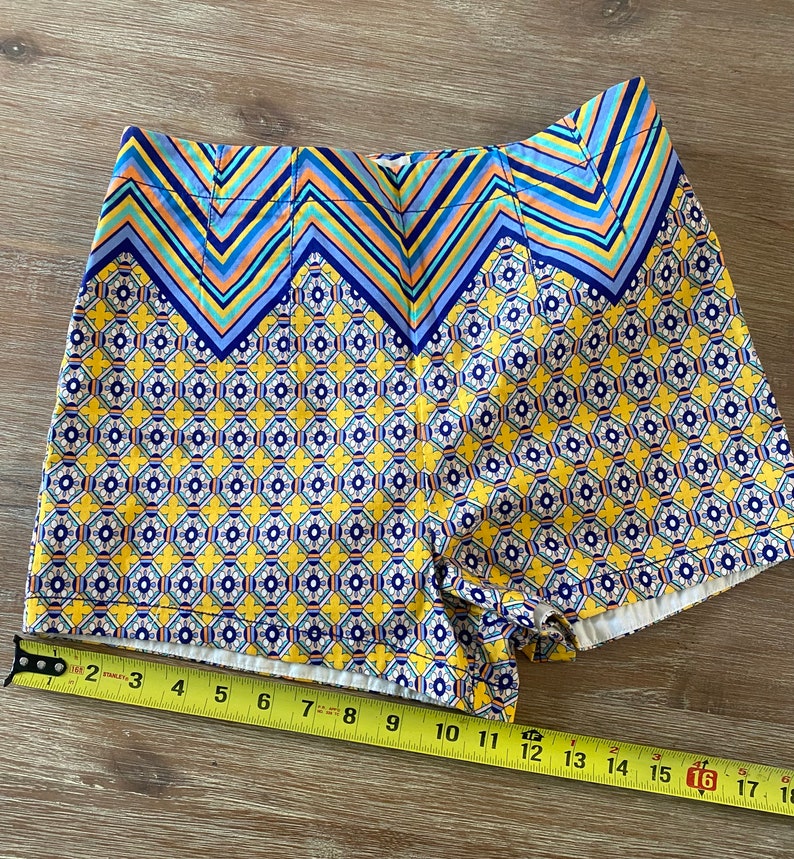May include: Yellow and blue patterned shorts with a geometric design. The shorts have a zig-zag pattern at the top and a smaller geometric pattern on the rest of the shorts.