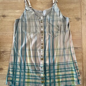 May include: A sleeveless plaid shirt with a button-up front and a pocket on the left side. The buttons are decorated with metal studs.