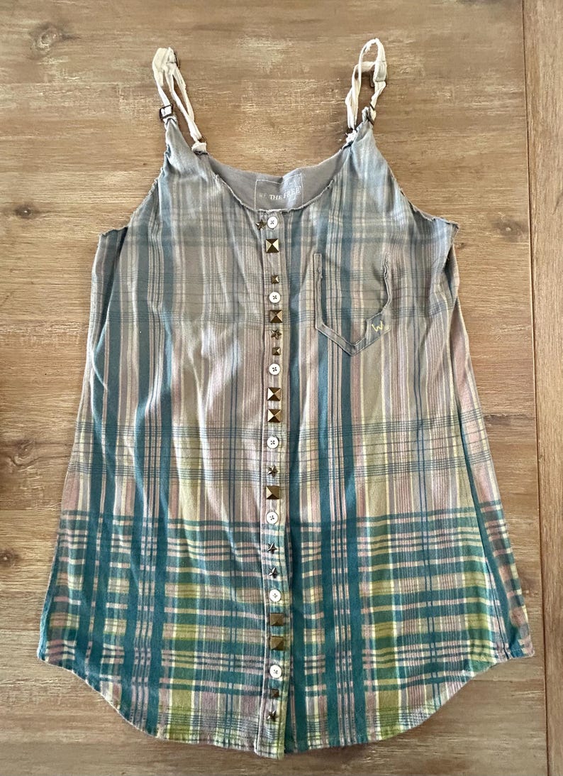May include: A sleeveless plaid shirt with a button-up front and a pocket on the left side. The buttons are decorated with metal studs.