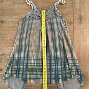 May include: A gray and blue plaid sleeveless top with a crocheted neckline and a high-low hem. The top has adjustable straps and a button closure at the back.