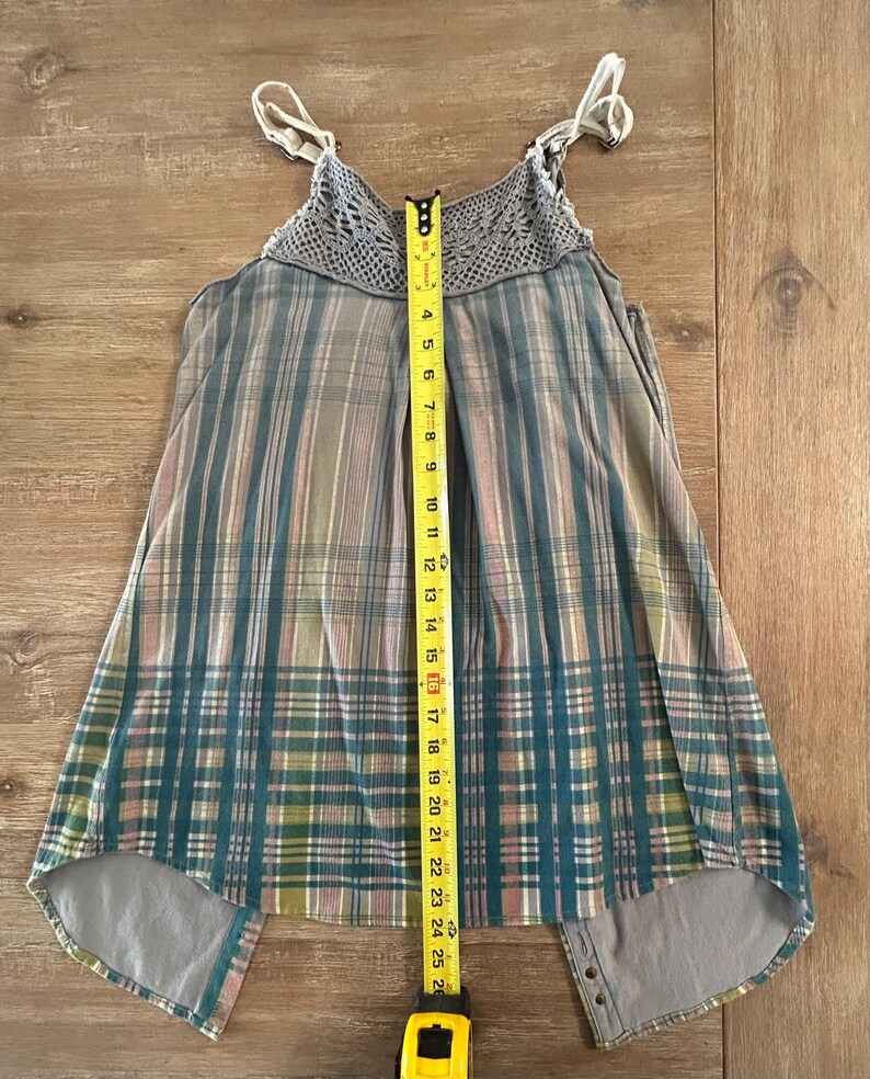May include: A gray and blue plaid sleeveless top with a crocheted neckline and a high-low hem. The top has adjustable straps and a button closure at the back.