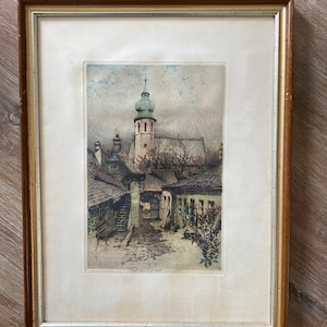 May include: A framed black and white print of a European village scene with a church steeple in the background. The print is in a brown wooden frame with a white mount.