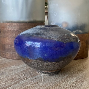 May include: A blue and brown ceramic vase with a speckled glaze. The vase has a rounded shape and a wide opening.