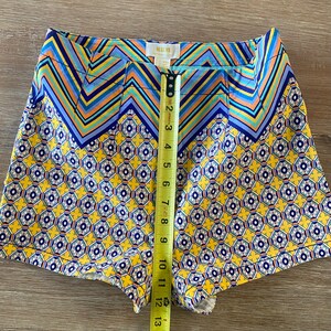 May include: Yellow and blue patterned shorts with a zig-zag pattern at the top and a smaller floral pattern on the bottom. The shorts have a waistband with a label that reads "Malva".