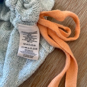 May include: A gray cotton blend fabric label with care instructions. The label says "Hand Wash Cold", "Do Not Wring or Twist", "Use Only Non-Chlorine Bleach", "Reshape & Lay Flat to Dry", "Low Iron as Needed", and "Do Not Dry Clean".