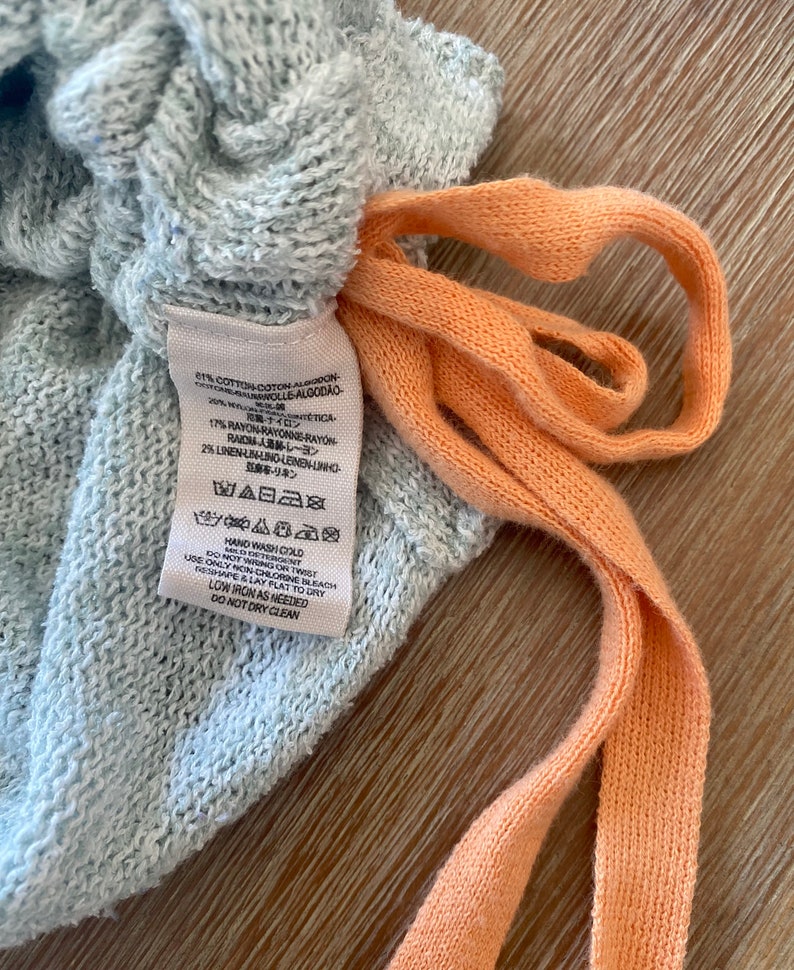 May include: A gray cotton blend fabric label with care instructions. The label says "Hand Wash Cold", "Do Not Wring or Twist", "Use Only Non-Chlorine Bleach", "Reshape & Lay Flat to Dry", "Low Iron as Needed", and "Do Not Dry Clean".