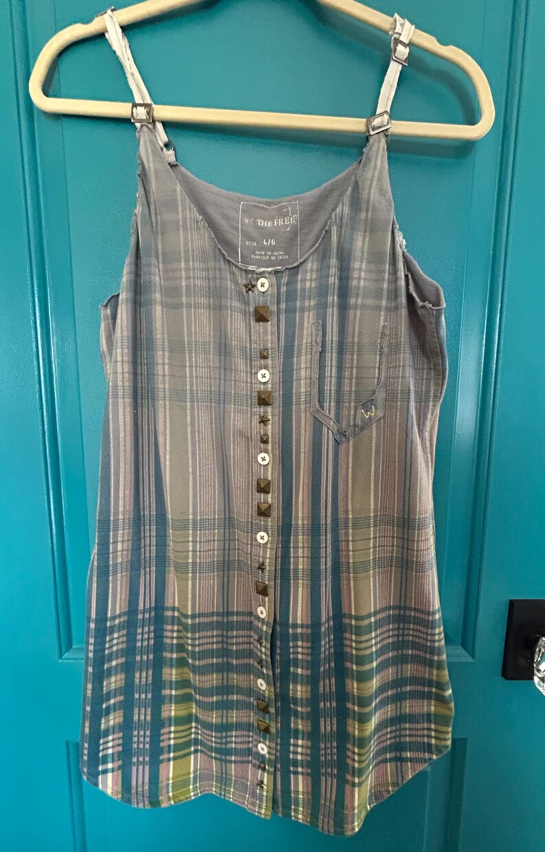 May include: A blue and gray plaid sleeveless dress with a button front and brown studded accents. The dress has a Free People tag with the size L/G.
