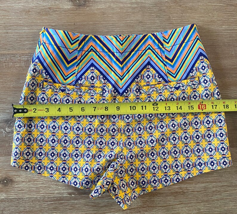 May include: Yellow, blue, and orange patterned shorts with a chevron pattern at the waistband. The shorts are made of a lightweight fabric and have a relaxed fit.