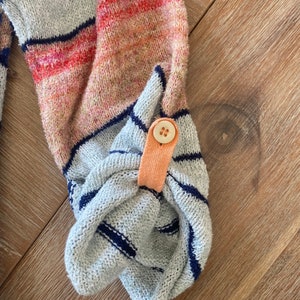 May include: Close-up of a gray and blue striped sweater with a peach-colored button detail on the cuff.