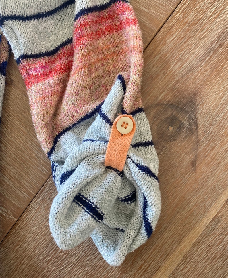 May include: Close-up of a gray and blue striped sweater with a peach-colored button detail on the cuff.
