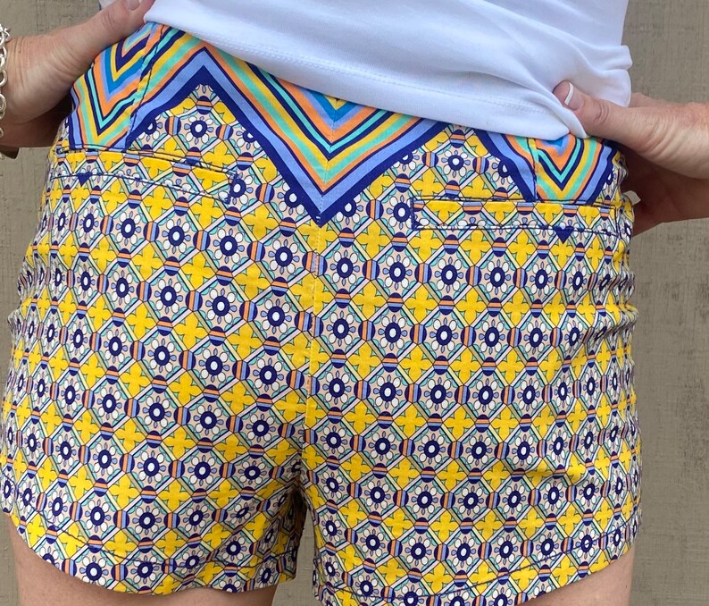 May include: Yellow and blue patterned shorts with a geometric design. The shorts have a waistband with a blue, green, and orange striped pattern.