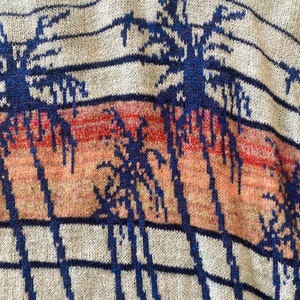 May include: A close-up of a knitted sweater with a palm tree pattern. The sweater is gray with blue and orange stripes. The palm trees are blue and are outlined in white.