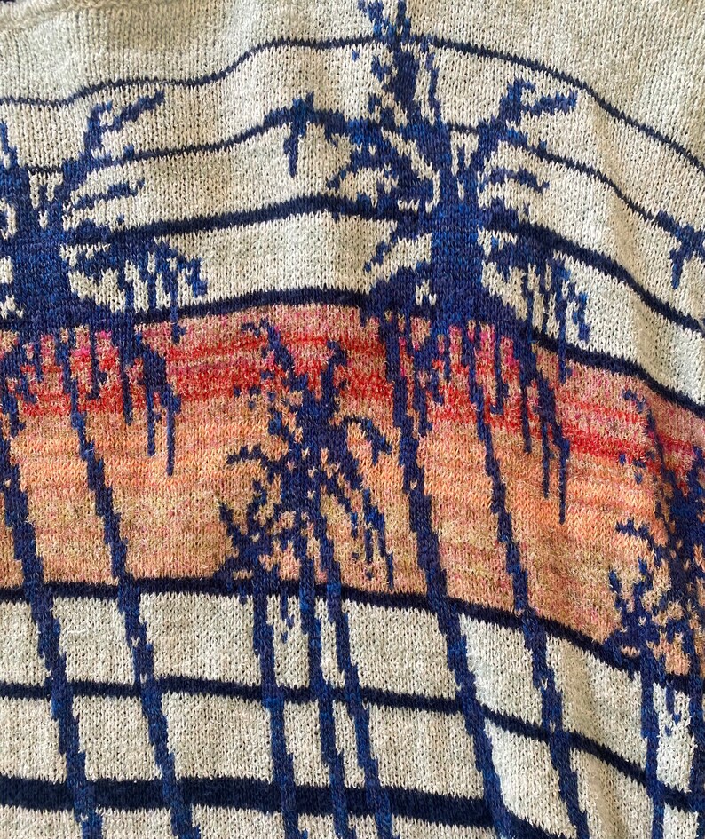 May include: A close-up of a knitted sweater with a palm tree pattern. The sweater is gray with blue and orange stripes. The palm trees are blue and are outlined in white.