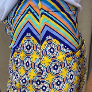 May include: A yellow skirt with a blue, orange, and white geometric pattern. The skirt has a zipper down the back.