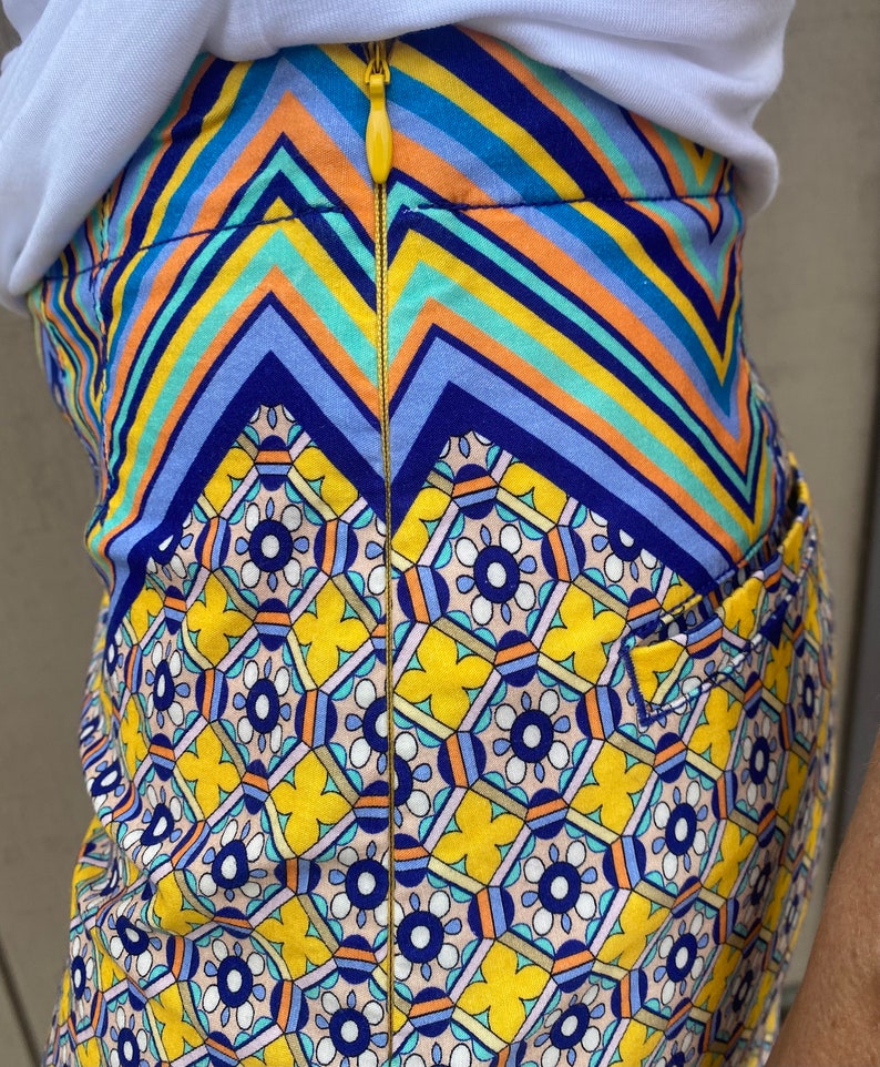 May include: A yellow skirt with a blue, orange, and white geometric pattern. The skirt has a zipper down the back.