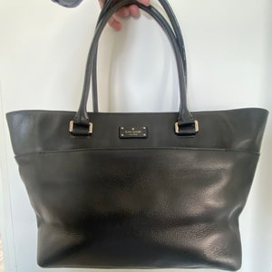 Cartera Kate Spade auténtica de segunda mano en cuero negro auténtico, dos asas, cierre de cremallera superior, bolso tote con forro de metal plateado y monograma negro