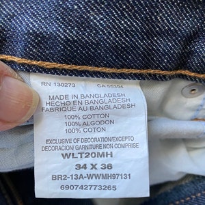 K&ouml;nnte beinhalten: Ein blaues Jeans-Etikett mit wei&szlig;em Text. Das Etikett enth&auml;lt den Text "RN 130273", "CA 55394", "Made in Bangladesh", "Hecho en Bangladesh", "Fabrique au Bangladesh", "100% Baumwolle", "100% Algodon", "100% Coton", "Exclusive of decoration/Excepto decoracion/ Garniture non comprise", "WLT20MH", "34 X 36", "BR2-13A-WWMH97131" und "690742773265".