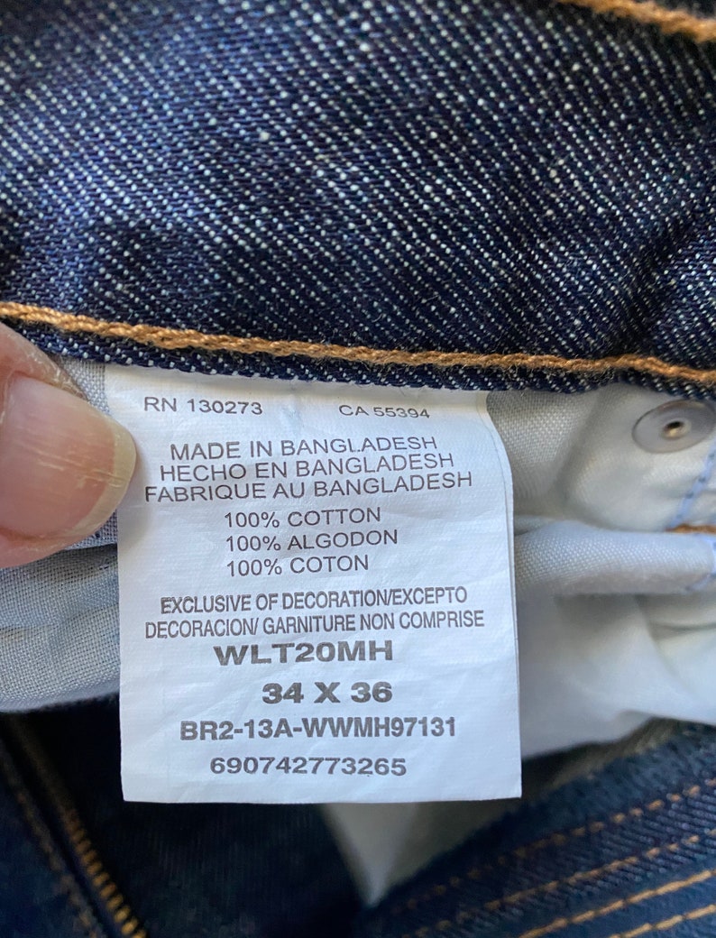 K&ouml;nnte beinhalten: Ein blaues Jeans-Etikett mit wei&szlig;em Text. Das Etikett enth&auml;lt den Text "RN 130273", "CA 55394", "Made in Bangladesh", "Hecho en Bangladesh", "Fabrique au Bangladesh", "100% Baumwolle", "100% Algodon", "100% Coton", "Exclusive of decoration/Excepto decoracion/ Garniture non comprise", "WLT20MH", "34 X 36", "BR2-13A-WWMH97131" und "690742773265".