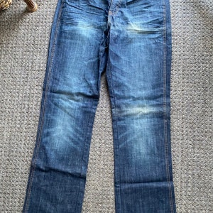 K&ouml;nnte beinhalten: Eine blaue Jeanshose mit Bootcut-Bein&ouml;ffnung. Die Jeans hat einen ausgewaschenen Look und ist von Wrangler.