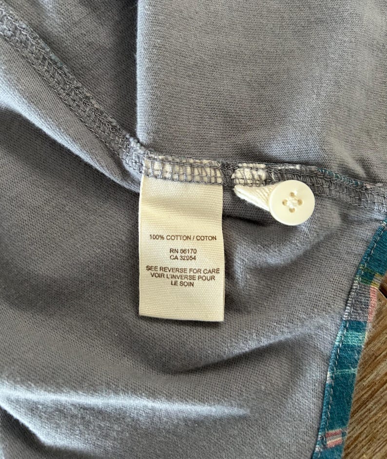 May include: A white tag with black text that reads "100% COTTON/COTON", "RN 66170", "CA 32054", "SEE REVERSE FOR CARE", "VOIR L'INVERSE POUR", "LE SOIN".