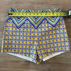 May include: Yellow, blue, and white patterned shorts with a geometric design. The shorts have a high waist and a wide waistband.