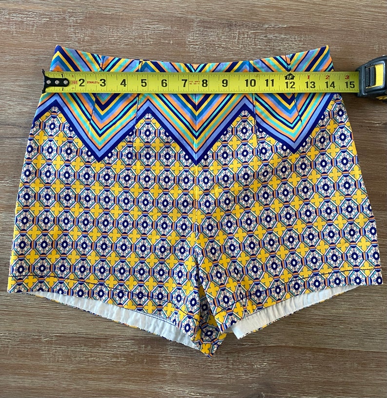 May include: Yellow, blue, and white patterned shorts with a geometric design. The shorts have a high waist and a wide waistband.