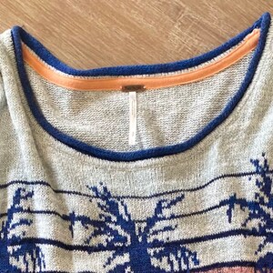 May include: Gray sweater with a blue and white palm tree pattern. The sweater has a blue and orange trim around the neckline.