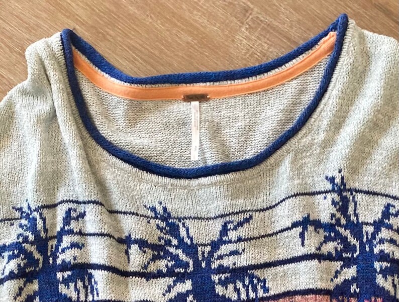 May include: Gray sweater with a blue and white palm tree pattern. The sweater has a blue and orange trim around the neckline.