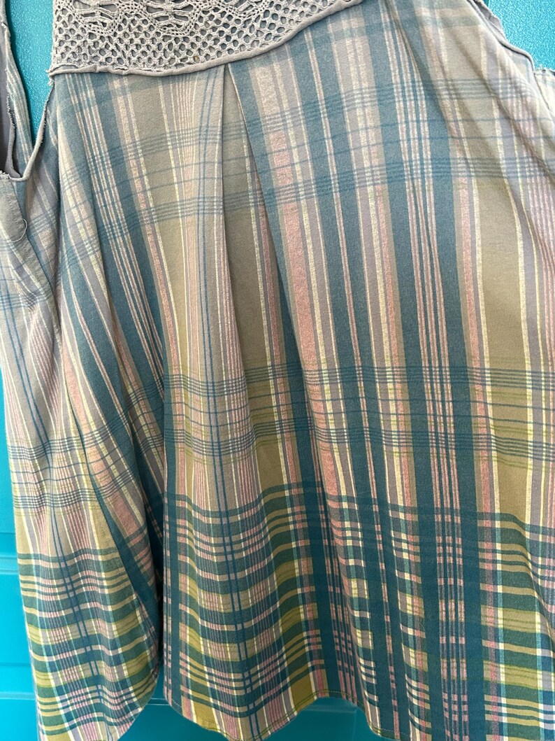 May include: A sleeveless top with a plaid pattern in shades of brown, green, and pink. The top has a crocheted trim at the neckline.