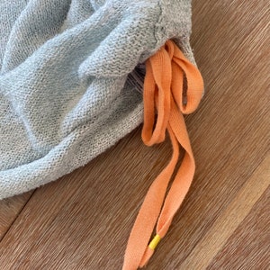 May include: Light blue sweatpants with a drawstring made of peach-colored fabric with yellow accents.