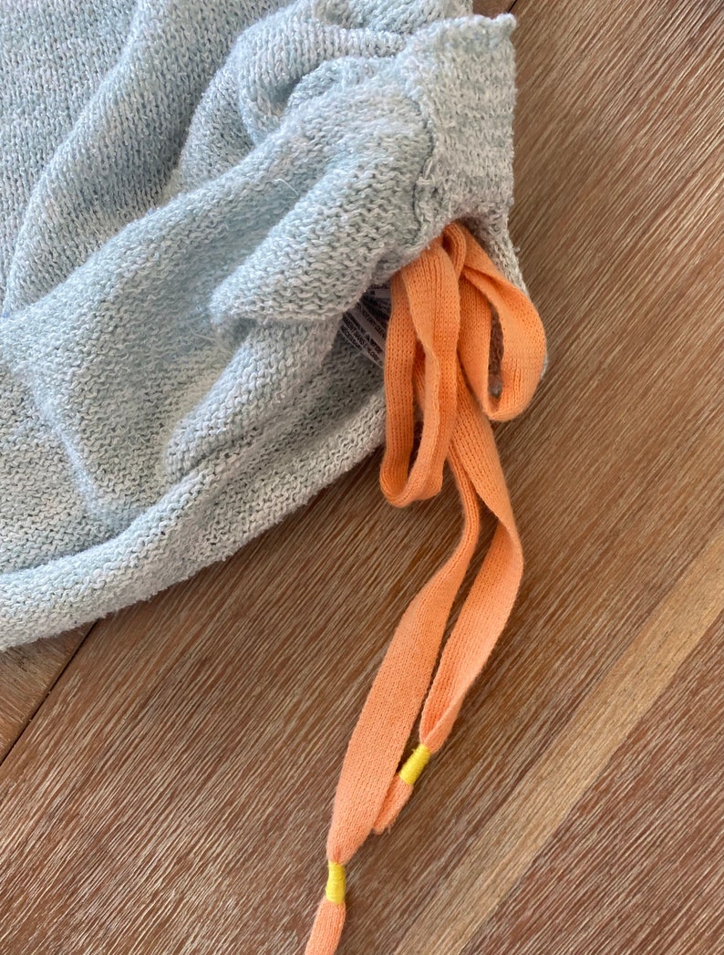 May include: Light blue sweatpants with a drawstring made of peach-colored fabric with yellow accents.