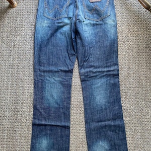 K&ouml;nnte beinhalten: Eine dunkelblaue Jeanshose mit einem braunen Leder-Patch auf der Ges&auml;&szlig;tasche, auf dem "Wrangler" steht.