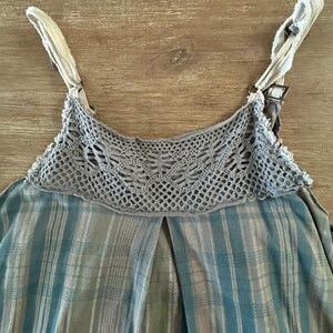 May include: A sleeveless plaid top with a crocheted trim around the neckline. The straps are white with a brown buckle.