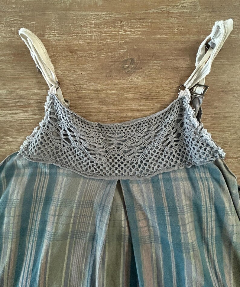May include: A sleeveless plaid top with a crocheted trim around the neckline. The straps are white with a brown buckle.