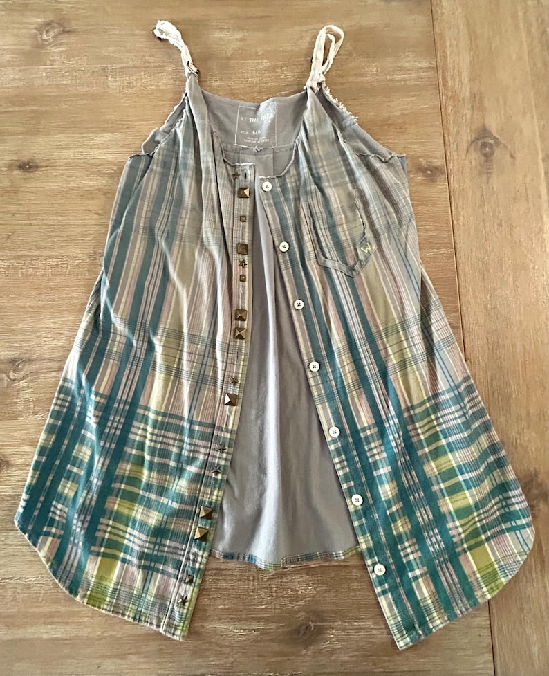 May include: A sleeveless plaid shirt dress with a gray tank top underneath. The dress has a button-up front and is decorated with metal studs.