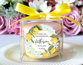 May include: A clear box with a yellow ribbon tied around it. Inside the box are two lemon-themed macarons with a sticker that says "Thank you for showering Katherine with love 11.29.25".