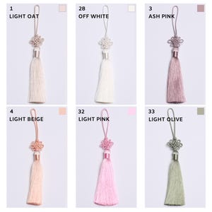 K&ouml;nnte beinhalten: Sechs dekorative Quasten mit Aufh&auml;ngeschlaufen und geknoteten Oberteilen, beschriftet mit Nummern und Farben: 1 Light Oat, 28 Off White, 3 Ash Pink, 4 Light Beige, 32 Light Pink und 33 Light Olive. Jede Quaste hat ein glattes, seidiges Fransenende.