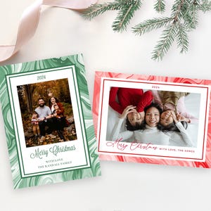 May include: Two Christmas cards with a marble design. The green card features a family of four sitting in a forest. The red card features a family of three lying on their backs. Both cards have the text "Merry Christmas" and the year "2024".