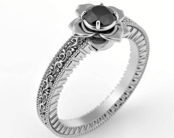 May include: A silver ring with a black gemstone set in a flower design. The band is intricately detailed with a floral pattern.