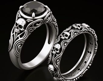 May include: Two silver rings with a gothic skull design. One ring features a large, black gemstone. Both rings have intricate scrollwork and skull details, set against a black background.