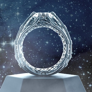 May include: A silver ring with a intricate, woven design. The ring is displayed on a white pedestal against a dark blue background with white stars.