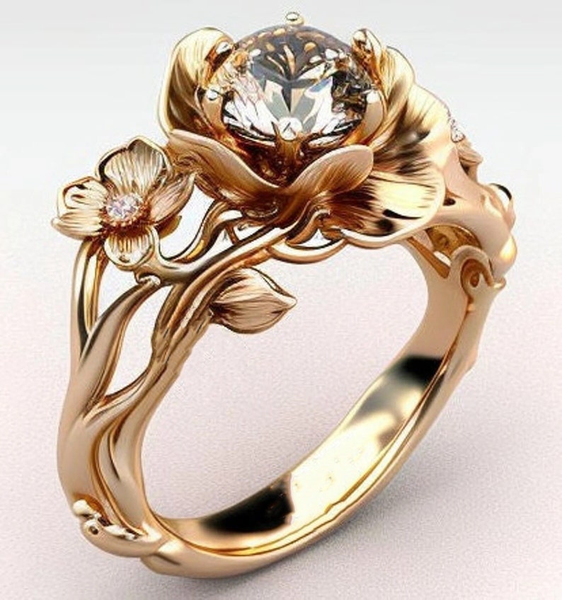 Op de afbeelding: Een gouden ring met een grote, heldere edelsteen gezet in een bloemmotief. De ring heeft ingewikkelde details en delicate bloemmotieven.