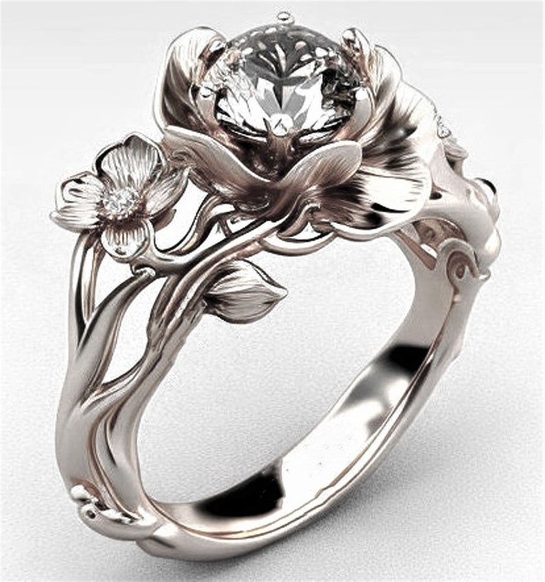 Op de afbeelding: Een zilveren ring met een grote, heldere edelsteen gezet in een bloemvormig ontwerp. De ring heeft ingewikkelde details en een delicaat bloemmotief.