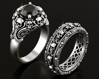 May include: Two silver rings with skull designs. One ring features a large black gemstone surrounded by skulls. The other ring is a band with a repeating skull pattern. Both rings have intricate detailing and a gothic aesthetic.