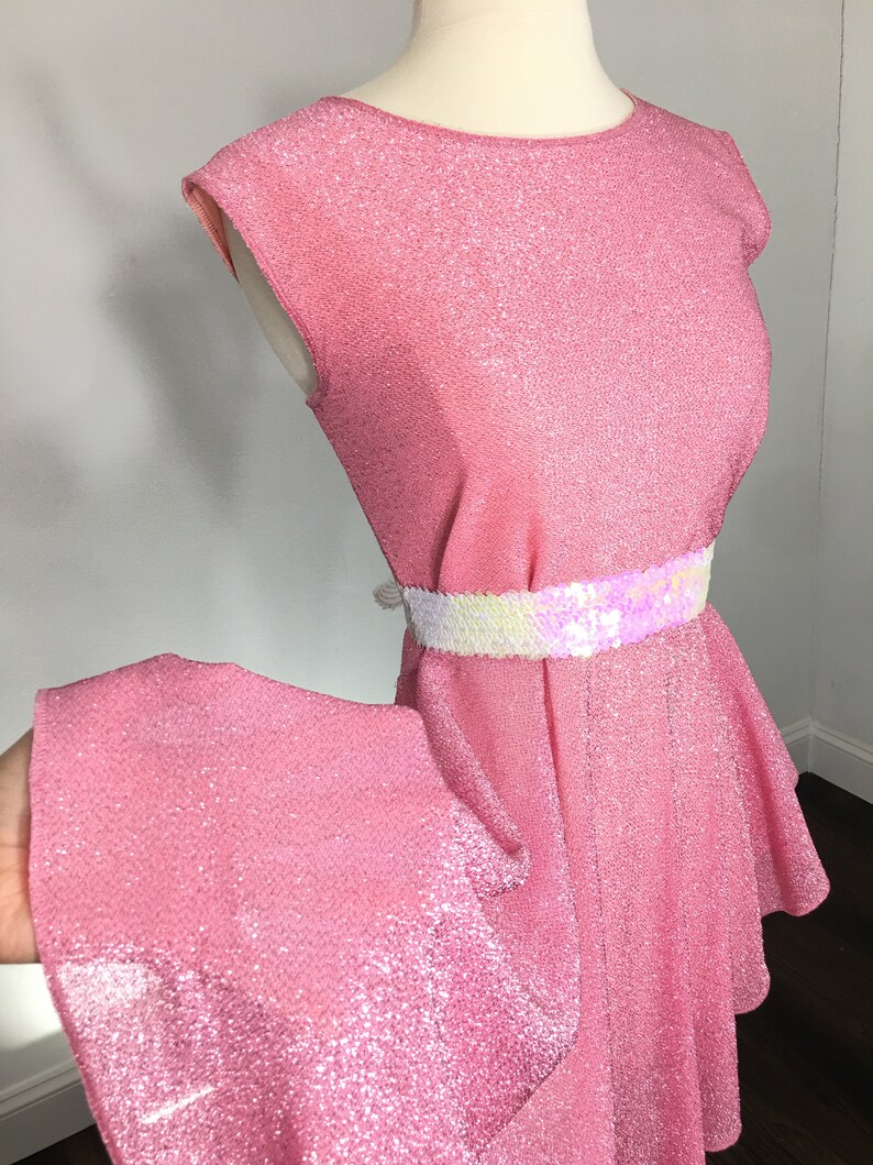 May include: A pink sparkly dress with a white and iridescent sequin belt. The dress has a ruffled skirt and a sleeveless bodice.