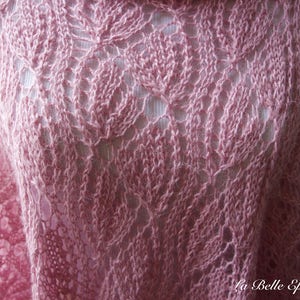 May include: A soft pink knitted shawl featuring an intricate openwork leaf pattern throughout the fabric. The garment displays a delicate, airy texture with visible yarn loops and a repeating botanical motif. The text La Belle Epoque Knits is visible.