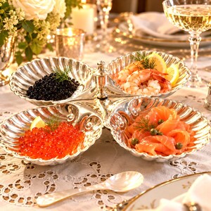 May include: A silver-plated four-section serving dish with a scalloped shell design. The dish holds black caviar, cooked shrimp with lemon slices, red salmon roe, and smoked salmon slices with capers, each garnished with a sprig of fresh dill.