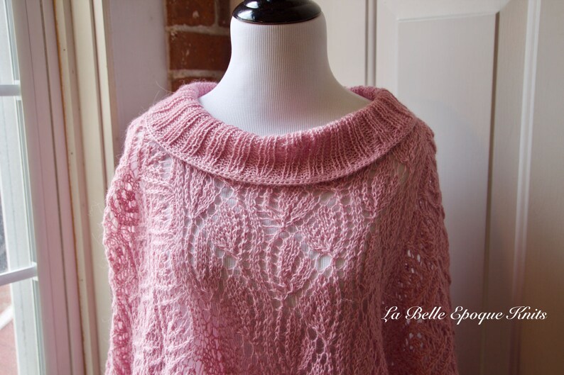 May include: A light pink knitted poncho featuring an intricate openwork leaf pattern and a wide ribbed collar. The garment displays a delicate texture throughout the knit. The text La Belle Epoque Knits is visible in the lower right corner.
